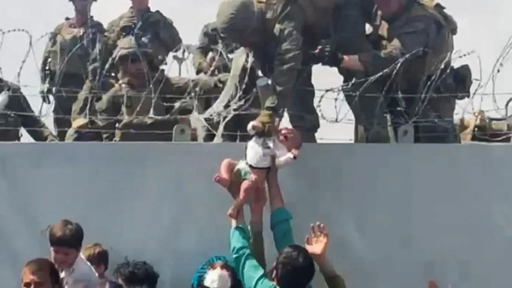 Un bebé afgano es entregado por encima de un muro en Kabul a soldados de EEUU