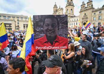 An opposer of Colombian President Gustavo Petro holds a banner with an image combining half of the faces of late Venezuelan President Hugo Chavez (L) and Petro, reading "Petro is Chavez" during a demonstration against government reforms in Bogota, on February 15, 2023. (Photo by JUAN BARRETO / AFP)