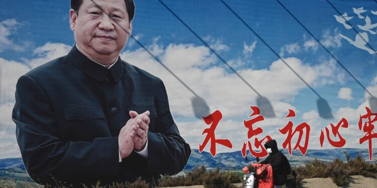 En esta foto de archivo tomada el 28 de febrero de 2023, un hombre pasa en scooter frente a una valla publicitaria que muestra al presidente de China, Xi Jinping, con un eslogan que dice "Permanecer fieles a nuestra aspiración original y tener nuestra misión firmemente en mente" en Beijing. - El líder de China, Xi Jinping, se deslizará hacia su tercer mandato en el poder magullado pero imperturbable por las protestas masivas, la ola mortal de Covid y el malestar económico que han afectado a su gobierno en los últimos meses. (Foto de Jade Gao / AFP)