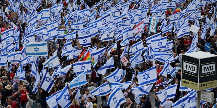 Los manifestantes se reúnen con banderas nacionales frente al parlamento de Israel en Jerusalén en medio de manifestaciones en curso y llamamientos a una huelga general contra el controvertido impulso del gobierno de extrema derecha para reformar el sistema de justicia, el 27 de marzo de 2023. (Foto de AHMAD GHARABLI / AFP)