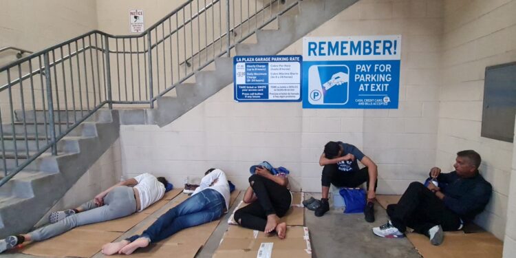 Un grupo de migrantes, en su mayoría provenientes de Venezuela, intentan descansar en un estacionamiento luego de ser liberados por agentes de Aduanas y Protección Fronteriza, en Brownsville, Texas, el 6 de mayo de 2023.