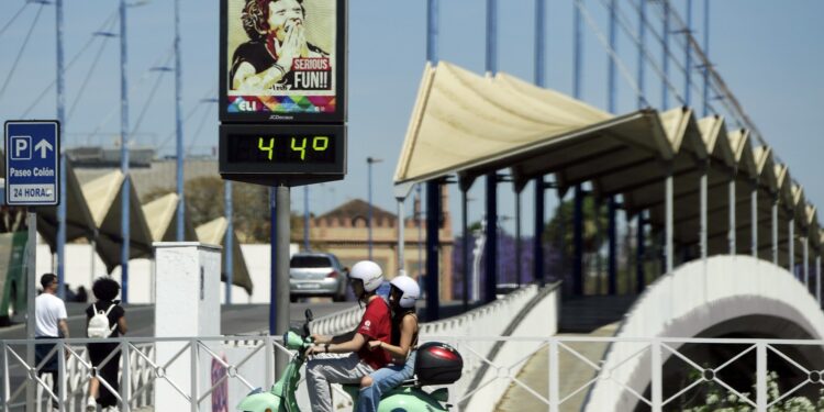 (ARCHIVOS) En esta foto de archivo tomada el 26 de abril de 2023, una pareja conduce una motocicleta Vespa frente a un termómetro callejero que marca 44 grados centígrados en Sevilla en medio de una ola de calor temprana. - El calor extremo que asoló la península ibérica y partes del norte de África la semana pasada habría sido "casi imposible sin el cambio climático", según constató un estudio científico internacional el 5 de mayo de 2023. (Foto de CRISTINA QUICLER / AFP)