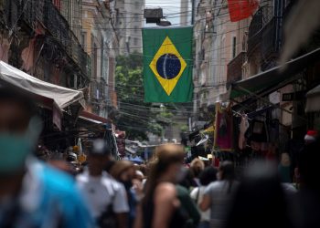 La gente camina en el mercado de Saara bajo una bandera brasileña en el centro de Río de Janeiro, Brasil, el 8 de diciembre de 2020, en medio de la pandemia del coronavirus (COVID-19). - Brasil, el país más poblado de América Latina, tenía 203,1 millones de habitantes en 2022, unos 10 millones menos de lo estimado, según datos del último censo difundido el 28 de junio de 2023 por el instituto oficial de estadística (IBGE). En el estudio demográfico realizado el año pasado se contabilizaron un total de 203.062.512 habitantes. (Foto por Mauro PIMENTEL / AFP)