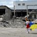 A child runs as she holds a Ukranian flag in front of the destroyed building of a cultural centre, hit in a missile strike, during a graduation ceremony of art students, in the town of Derhachi, Kharkiv region, on June 17, 2023. (Photo by Sergey BOBOK / AFP)