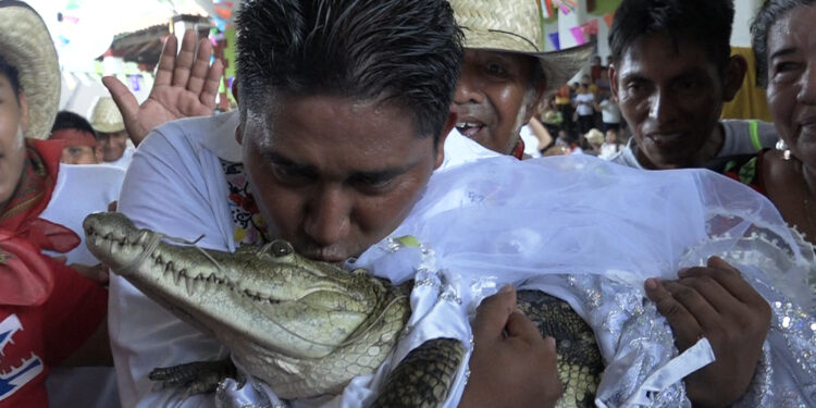 Victor Hugo Sosa, Mayor of San Pedro Huamelula, kisses a spectacled caiman (Caiman crocodilus) called "La Niña Princesa" ("The Princess Girl") before marrying her in San Pedro Huamelula, Oaxaca state, Mexico on June 30, 2023. - This ancient ritual of more than 230 years unites two ethnic groups in marriage to bring prosperity and peace. The spectacled caiman (Caiman crocodilus) is paraded around the community before being dressed as a bride and marrying the Mayor. According to beliefs, this union between the human and the divine will bring blessings such as a good harvest and abundant fishing. (Photo by RUSVEL RASGADO / AFP)