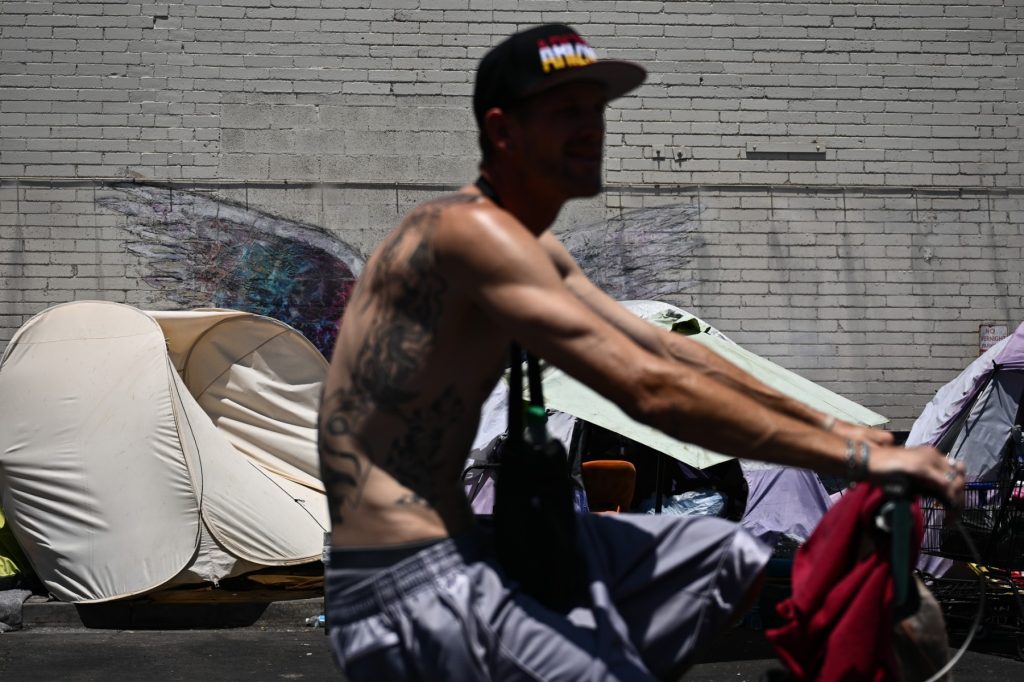 Un ciclista pasa junto a personas que acampan en "The Zone", un vasto campamento para personas sin hogar donde residen cientos de personas, durante una ola de calor récord en Phoenix, Arizona, el 18 de julio de 2023.