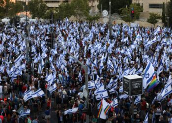 Los manifestantes ondean banderas israelíes mientras marchan hacia Jerusalén el 22 de julio de 2023, durante una marcha de varios días que comenzó en Tel Aviv para protestar contra el proyecto de ley de reforma judicial del gobierno antes de una votación en el parlamento. - Israel se ha visto sacudido por una ola de protestas de meses después de que el gobierno revelara en enero planes para reformar el sistema judicial que, según los opositores, amenazan la democracia del país. (Foto de HAZEM BADER / AFP)