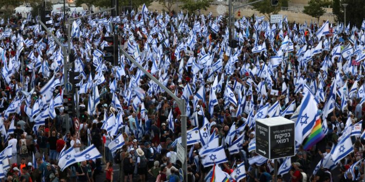 Los manifestantes ondean banderas israelíes mientras marchan hacia Jerusalén el 22 de julio de 2023, durante una marcha de varios días que comenzó en Tel Aviv para protestar contra el proyecto de ley de reforma judicial del gobierno antes de una votación en el parlamento. - Israel se ha visto sacudido por una ola de protestas de meses después de que el gobierno revelara en enero planes para reformar el sistema judicial que, según los opositores, amenazan la democracia del país. (Foto de HAZEM BADER / AFP)