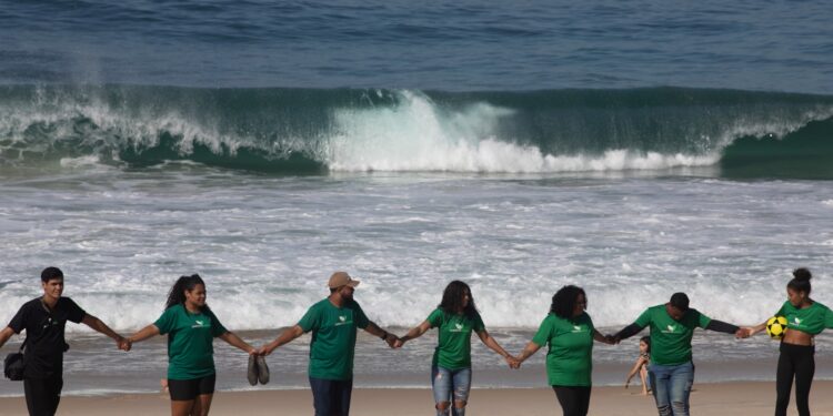 Voluntarios de una Organización No Gubernamental se dan la mano después de limpiar la playa de Sao Conrado en Río de Janeiro, Brasil, el 8 de junio de 2023 en el marco del Día Mundial de los Océanos. (Foto de Joao Laet / AFP)