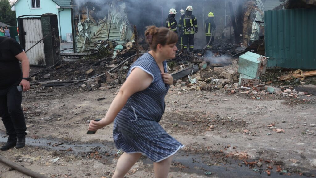 Una mujer pasa junto a los bomberos que apagan un incendio en una casa que resultó dañada tras un ataque con misiles en una aldea en las afueras de Kiev el 30 de agosto de 2023, en medio de la invasión rusa de Ucrania. (Foto de Anatolii STEPANOV / AFP)