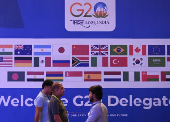 People walk past a banner with flags of countries participating in G20 summit at the International Media Center (IMC) at G20 venue on the eve of the two-day G20 summit in New Delhi on September 8, 2023. (Photo by TAUSEEF MUSTAFA / AFP)