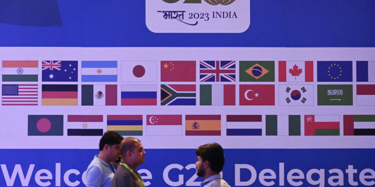 People walk past a banner with flags of countries participating in G20 summit at the International Media Center (IMC) at G20 venue on the eve of the two-day G20 summit in New Delhi on September 8, 2023. (Photo by TAUSEEF MUSTAFA / AFP)