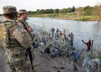 Members of the National Guard look on as migrants try to find a way past razor wire in Eagle Pass, Texas, on September 24, 2023. - Dozens of migrants arrived at the US-Mexico border September 22, hoping to be allowed into the United States, with US border forces reporting 1.8 million encounters with migrants in the last 12 months. (Photo by ANDREW CABALLERO-REYNOLDS / AFP)