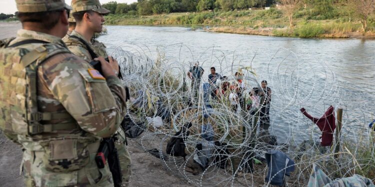 Members of the National Guard look on as migrants try to find a way past razor wire in Eagle Pass, Texas, on September 24, 2023. - Dozens of migrants arrived at the US-Mexico border September 22, hoping to be allowed into the United States, with US border forces reporting 1.8 million encounters with migrants in the last 12 months. (Photo by ANDREW CABALLERO-REYNOLDS / AFP)