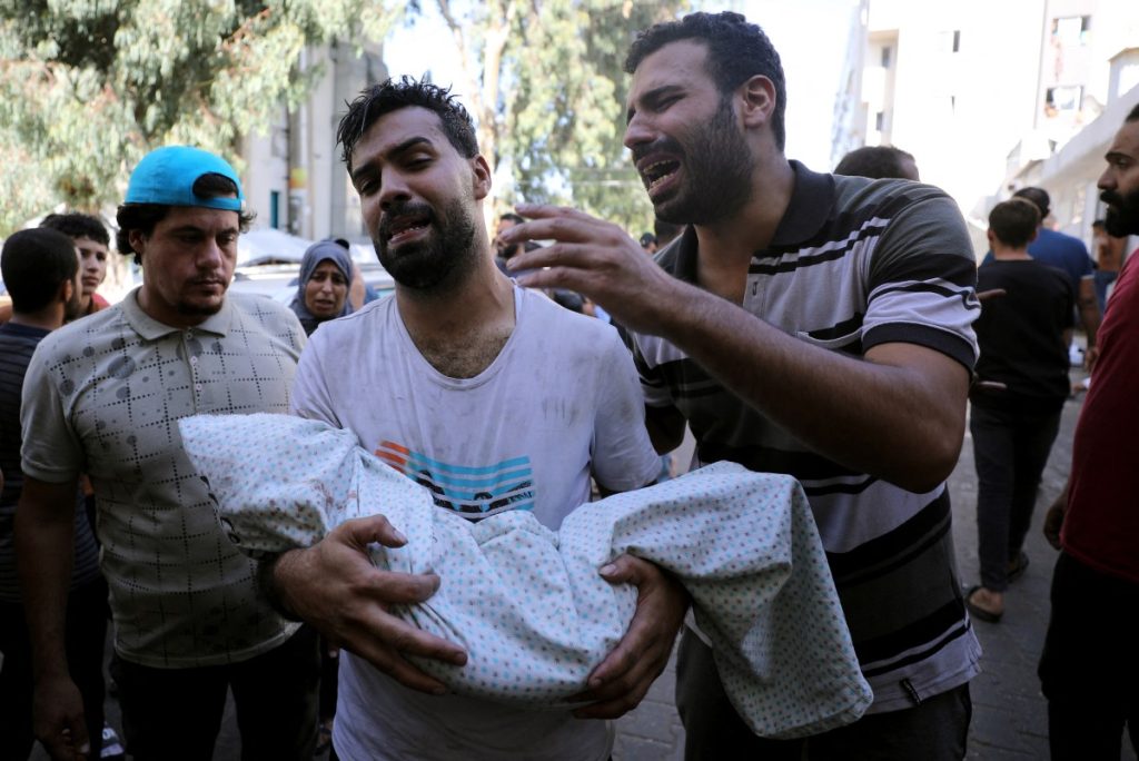 NOTA DEL EDITOR: Contenido gráfico / Un palestino sostiene el cuerpo de un niño envuelto en una mortaja mientras otro reacciona junto a él, afuera de un hospital luego del bombardeo israelí del suburbio oriental de Shujaiya en la ciudad de Gaza el 4 de noviembre de 2023, en medio de las batallas en curso entre Israel. y el grupo palestino Hamás. - Los combates estallaron en Gaza el 4 de noviembre, día 29 desde que militantes de Hamás irrumpieron en la frontera israelí y, según funcionarios israelíes, mataron a 1.400 personas, en su mayoría civiles, y secuestraron a más de 240 personas más. Desde entonces, Israel ha bombardeado implacablemente la Franja de Gaza y ha enviado tropas terrestres, y el Ministerio de Salud en el territorio palestino gobernado por Hamás dice que 9.488 personas han muerto, alrededor de dos tercios de ellas mujeres y niños. (Foto de Dawood NEMER / AFP)