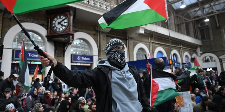 A protester waves a Palestinian flag as people take part in a sit-down protest inside Charing Cross station following the 'London Rally For Palestine' in, central London on November 4, 2023, as they call for a ceasefire in the conflict between Israel and Hamas. - Thousands of civilians, both Palestinians and Israelis, have died since October 7, 2023, after Palestinian Hamas militants based in the Gaza Strip entered southern Israel in an unprecedented attack triggering a war declared by Israel on Hamas with retaliatory bombings on Gaza. (Photo by JUSTIN TALLIS / AFP)