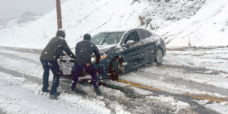 Los residentes locales intentan evitar que un automóvil se deslice por una carretera helada durante una tormenta de nieve en Rancho Cucamonga, California, el 25 de febrero de 2023. Cayeron fuertes nevadas en el sur de California cuando la primera tormenta de nieve en una generación azotó las colinas alrededor de Los Ángeles, con Fuertes lluvias que amenazan con inundaciones en otros lugares. (Foto de JOSH EDELSON / AFP)