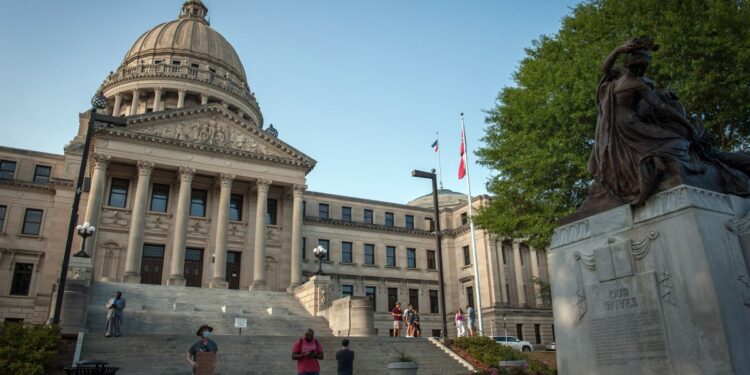 La gente se encuentra junto a la estatua de las Madres Confederadas (R) afuera del edificio del Capitolio del Estado de Mississippi durante la histórica votación de la legislatura estatal para cambiar la bandera de Mississippi en Jackson, Mississippi, el 28 de junio de 2020.