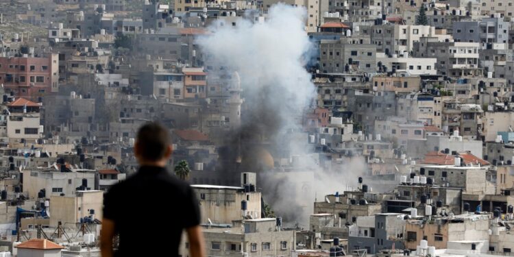 Un hombre observa cómo se eleva el humo sobre los edificios en el campo de refugiados palestinos de Nur Shams, cerca de la ciudad ocupada de Tulkarm, en Cisjordania, durante una incursión israelí en curso el 4 de enero de 2024. (Foto de Zain JAAFAR / AFP)