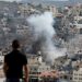 Un hombre observa cómo se eleva el humo sobre los edificios en el campo de refugiados palestinos de Nur Shams, cerca de la ciudad ocupada de Tulkarm, en Cisjordania, durante una incursión israelí en curso el 4 de enero de 2024. (Foto de Zain JAAFAR / AFP)