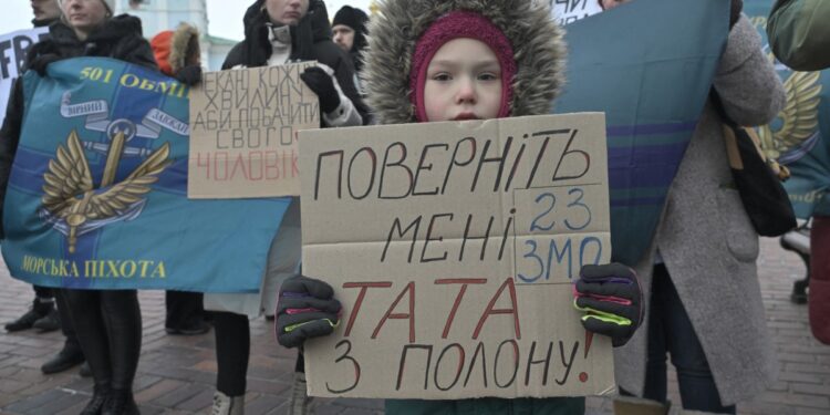 Un niño sostiene un cartel que dice "Traer a mi padre del cautiverio" mientras familiares de prisioneros de guerra militares ucranianos exigen su liberación durante una manifestación en Kiev, el 7 de enero de 2024, en medio de la invasión rusa de Ucrania. (Foto de Genya SAVILOV / AFP)