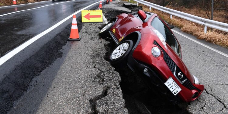 El tráfico (L) pasa por una carretera recién pavimentada junto a un automóvil que permanece atrapado en la antigua acera en la ciudad de Anamizu, prefectura de Ishikawa, el 6 de enero de 2024, después de que un gran terremoto de magnitud 7,5 sacudiera la región de Noto el día de Año Nuevo. . (Foto de Toshifumi KITAMURA / AFP)