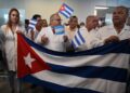 Médicos cubanos sostienen una bandera nacional a su llegada al Aeropuerto Internacional de Palmerola, a 50 kilómetros al norte de Tegucigalpa, el 27 de febrero de 2024. - La brigada de 100 médicos especialistas permanecerá en Honduras durante dos años e incluye anestesiólogos, oncólogos, neurocirujanos, cardiólogos y endocrinólogos. (Foto de Orlando SIERRA / AFP)