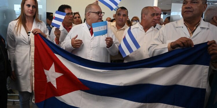 Médicos cubanos sostienen una bandera nacional a su llegada al Aeropuerto Internacional de Palmerola, a 50 kilómetros al norte de Tegucigalpa, el 27 de febrero de 2024. - La brigada de 100 médicos especialistas permanecerá en Honduras durante dos años e incluye anestesiólogos, oncólogos, neurocirujanos, cardiólogos y endocrinólogos. (Foto de Orlando SIERRA / AFP)