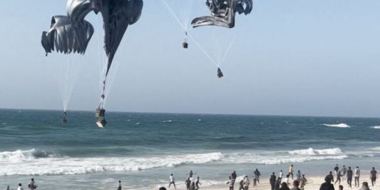 This image grab from an AFPTV video shows Palestinians running toward parachutes attached to food parcels, air-dropped from US aircrafts on a beach in the Gaza Strip on March 2, 2024. - Israel's top ally the United States said it began air-dropping aid into war-ravaged Gaza on March 2, as the Hamas-ruled territory's health ministry reported more than a dozen child malnutrition deaths. (Photo by AFP)