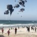 This image grab from an AFPTV video shows Palestinians running toward parachutes attached to food parcels, air-dropped from US aircrafts on a beach in the Gaza Strip on March 2, 2024. - Israel's top ally the United States said it began air-dropping aid into war-ravaged Gaza on March 2, as the Hamas-ruled territory's health ministry reported more than a dozen child malnutrition deaths. (Photo by AFP)