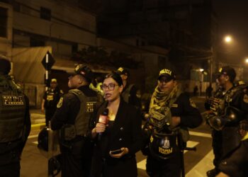 A reporter speaks as police guard outside President Dina Boluarte's house during a raid ordered by the Attorney General's Office as part of a preliminary investigation in Lima on March 30, 2024. - Peruvian authorities raided President Dina Boluarte's home on March 30 as part of an ongoing corruption investigation related to undisclosed luxury watches. (Photo by Juan Carlos CISNEROS / AFP)