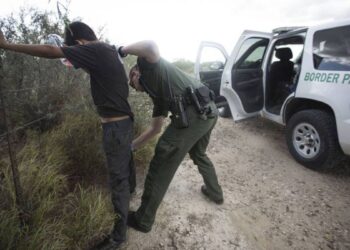 Policía fronteriza requisando migrantes en las fronteras.