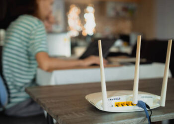 Una mujer trabaja en casa usando un módem enrutador, conectando Internet a su computadora portátil.