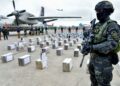 In this handout picture released by the Peruvian Ministry of Interior, an anti-drug police stand guard stands next to more than 3 tons of cocaine packed in bricks on the tarmac of a military air base in Callao, a province adjacent to Lima, on October 24, 2023. Peru's anti-drug police announced Tuesday the seizure of three tons of cocaine destined for the United States, in an operation in which three Ecuadorians and a Colombian were also arrested. (Photo by Handout / Peru's Interior Ministry / AFP) / RESTRICTED TO EDITORIAL USE - MANDATORY CREDIT "AFP PHOTO / PERU'S INTERIOR MINISTRY" - NO MARKETING - NO ADVERTISING CAMPAIGNS - DISTRIBUTED AS A SERVICE TO CLIENTS - RESTRICTED TO EDITORIAL USE - MANDATORY CREDIT "AFP PHOTO / Peru's Interior Ministry" - NO MARKETING - NO ADVERTISING CAMPAIGNS - DISTRIBUTED AS A SERVICE TO CLIENTS /