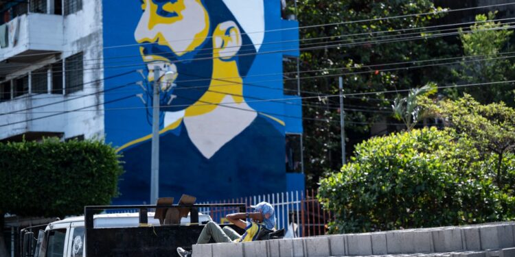 Un trabajador se apoya en bloques de cemento transportados por un camión que pasa junto a un mural que representa al presidente de El Salvador y candidato a la reelección por el partido Nuevas Ideas, Nayib Bukele, en el barrio Zacamil de San Salvador el 1 de febrero de 2024. - El Salvador va a las urnas el 4 de febrero. (Foto de Yuri CORTEZ / AFP)
