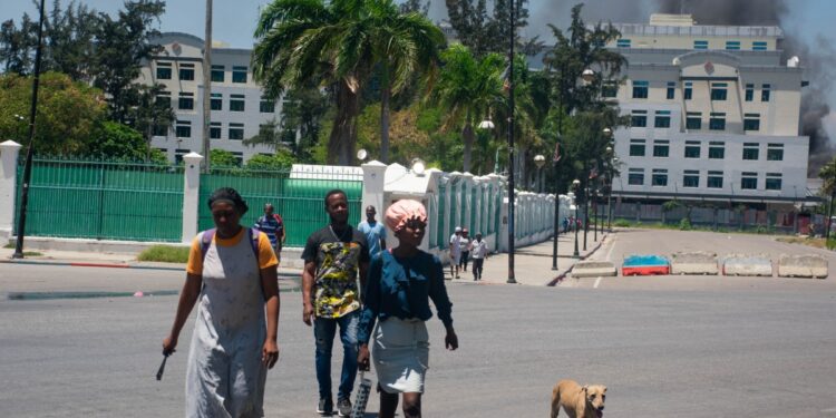Mientras el humo sale del edificio del Ministerio de Finanzas detrás de ellos, la gente abandona la zona después de escuchar disparos de bandas armadas cerca del Palacio Nacional en Puerto Príncipe, Haití, el 2 de abril de 2024. - Más de 50.000 personas huyeron de Puerto Príncipe -Prince dentro de tres semanas el mes pasado cuando una explosión de violencia de pandillas sacudió la capital haitiana, dijo Naciones Unidas el 2 de abril de 2024. (Foto de Clarens SIFFROY / AFP)