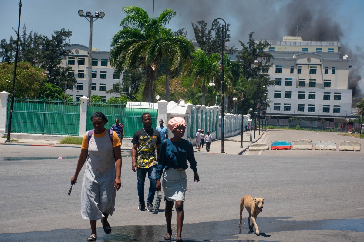 Mientras el humo sale del edificio del Ministerio de Finanzas detrás de ellos, la gente abandona la zona después de escuchar disparos de bandas armadas cerca del Palacio Nacional en Puerto Príncipe, Haití, el 2 de abril de 2024. - Más de 50.000 personas huyeron de Puerto Príncipe -Prince dentro de tres semanas el mes pasado cuando una explosión de violencia de pandillas sacudió la capital haitiana, dijo Naciones Unidas el 2 de abril de 2024. (Foto de Clarens SIFFROY / AFP)